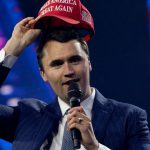 Charlie Kirk holding a MAGA hat above his head